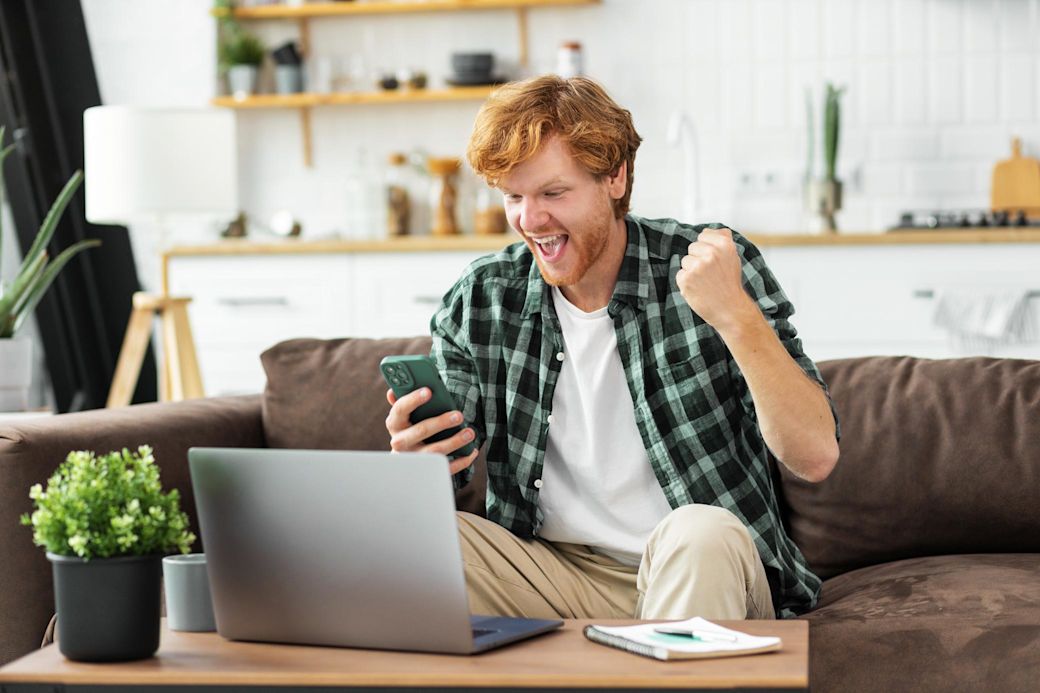 Mann sitzt im Wohnzimmer und freut sich über Gaswechsel per Handy