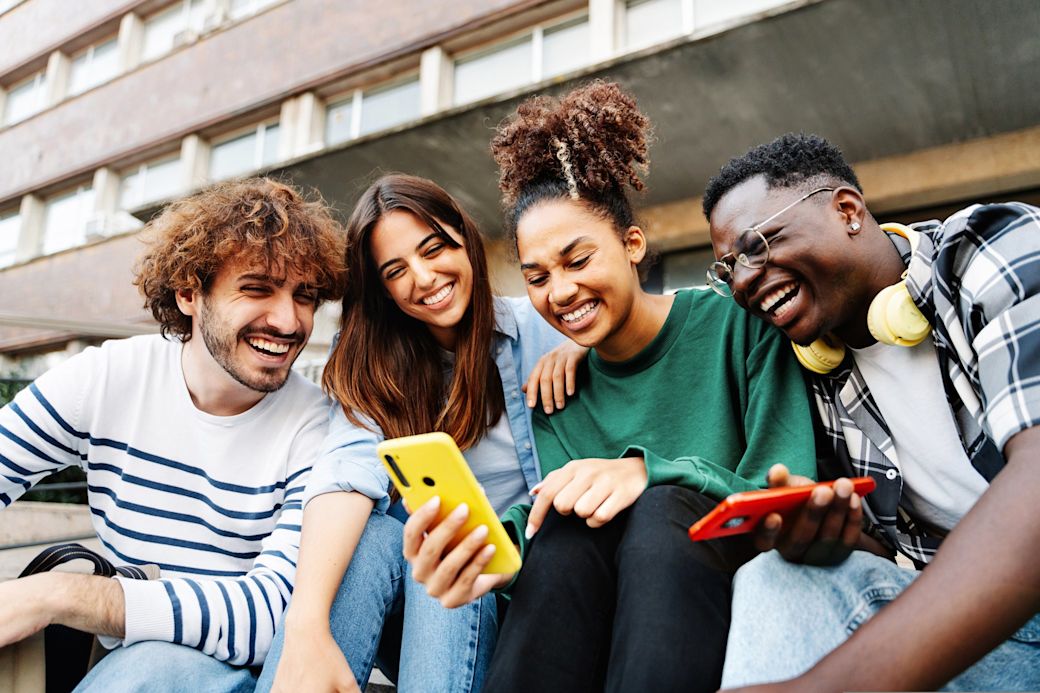 Strom und Gas für Studierende - total easy mit Yello 4 Freunde sitzen zusammen draußen vor einem Gebäude und schauen aufs Handy