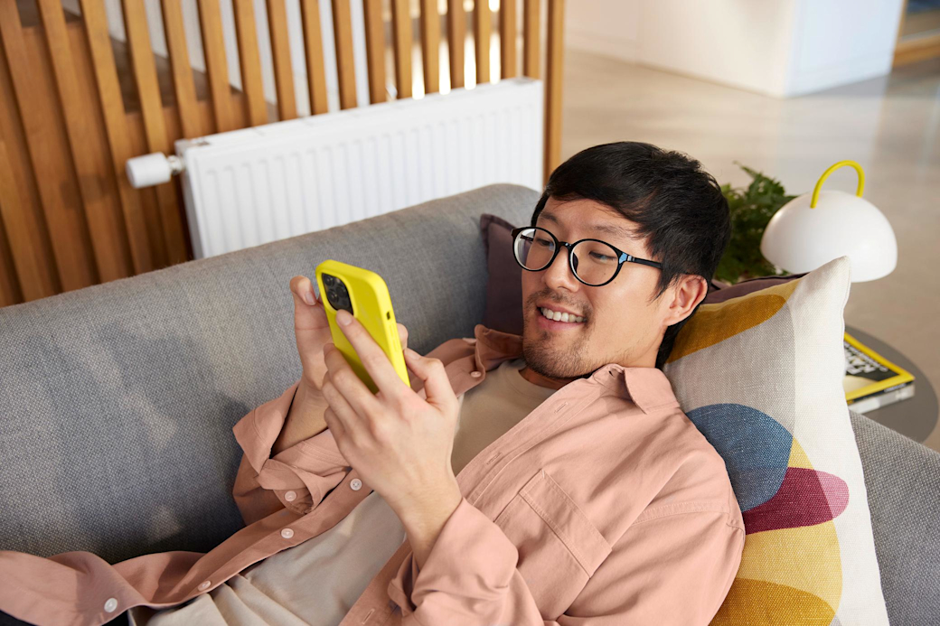 Vergleich deine Strom- und Gaspreise schnell Online Mann liegt auf der Couch vor der Heizung und schaut aufs Handy