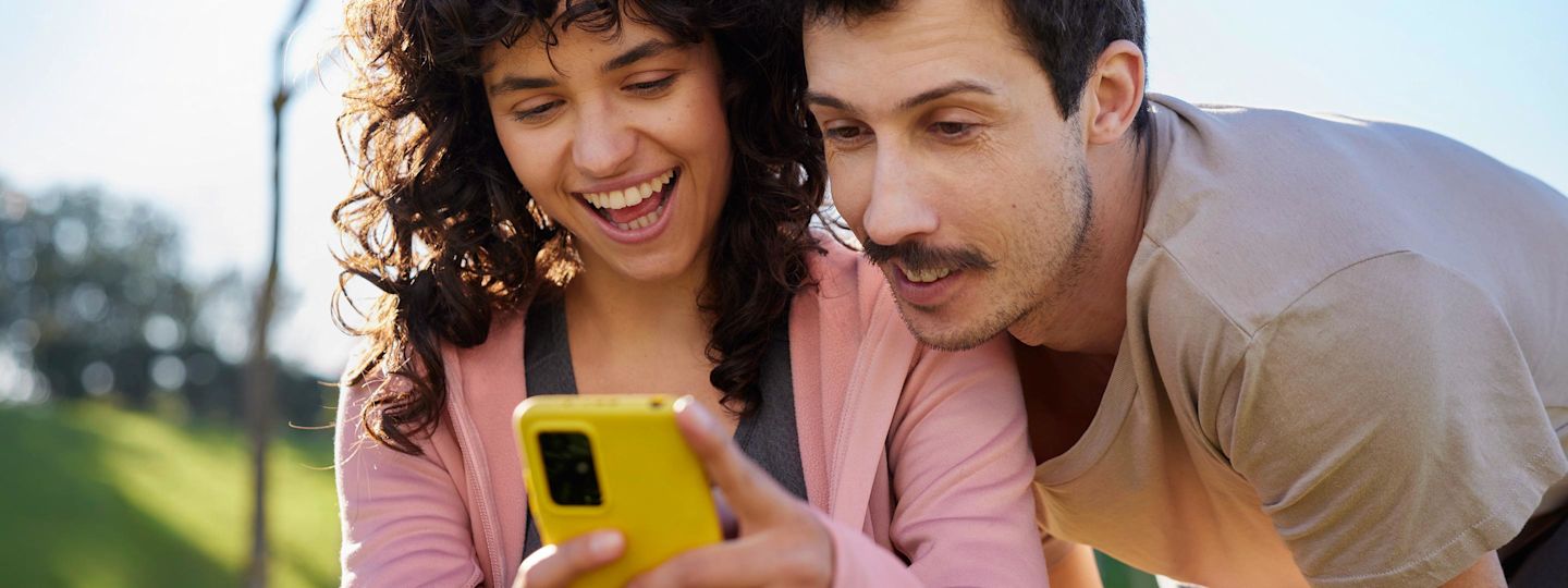 Frau und Mann schauen auf den Bildschirm eines gelben Smartphones.
