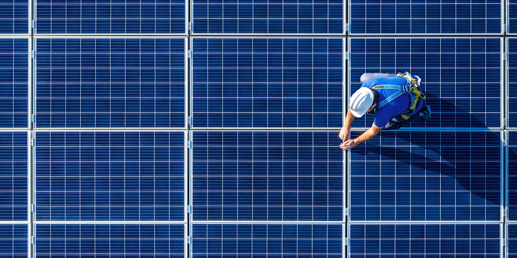 Ein Mann installiert blaue Solarmodule auf dem Dach.