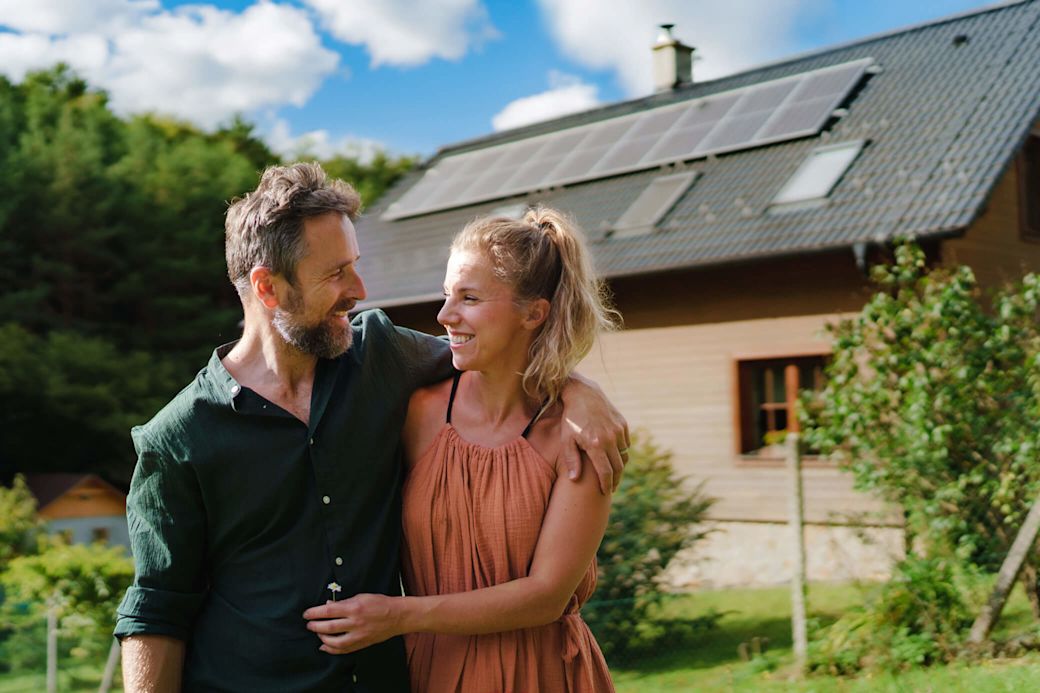 Mit einer Solaranlage zur Miete einfach zum eigenen Sonnenstrom Frau und Mann stehen Arm in Arm vor Haus mit Solaranlage