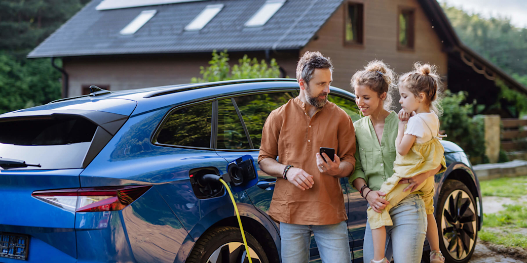 Familie mit Mädchen laden Elektroauto vor dem Haus