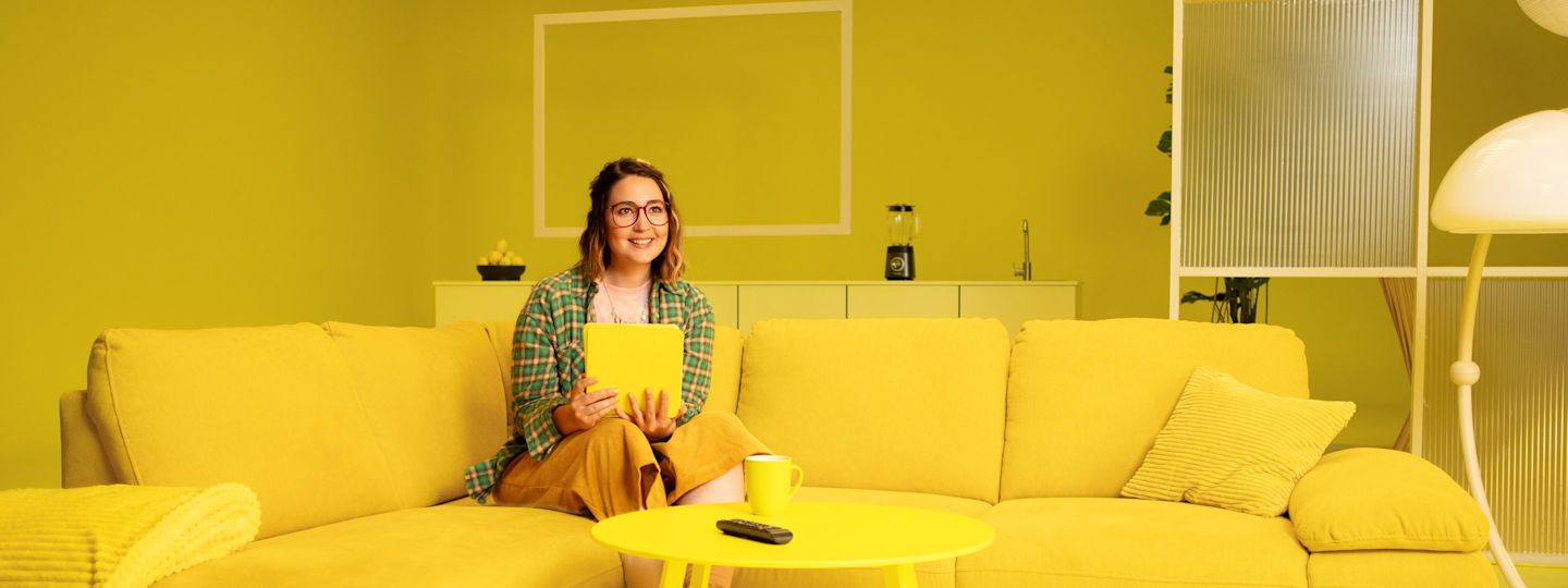 Unsere Yello Gas- und Heiztarife für dein warmes Zuhause. Junge Frau sitzt mit einem Tablet auf der Couch im Wohnzimmer