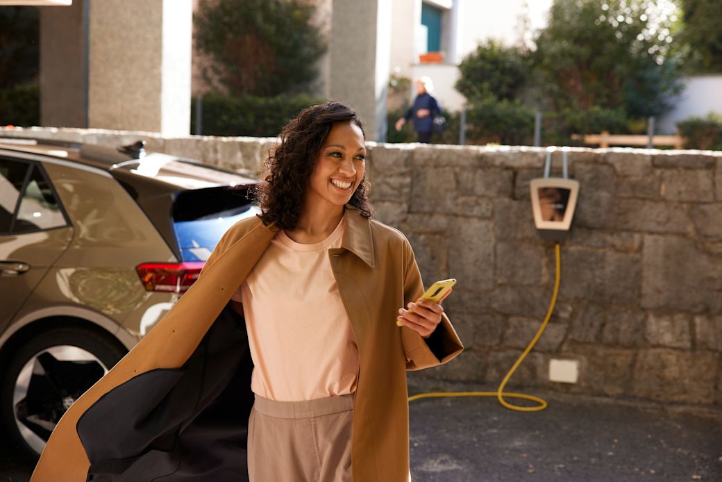 Energie die Spaß macht ist einfach smart Lachende Frau mit Handy lädt E-Auto über eine Wallbox