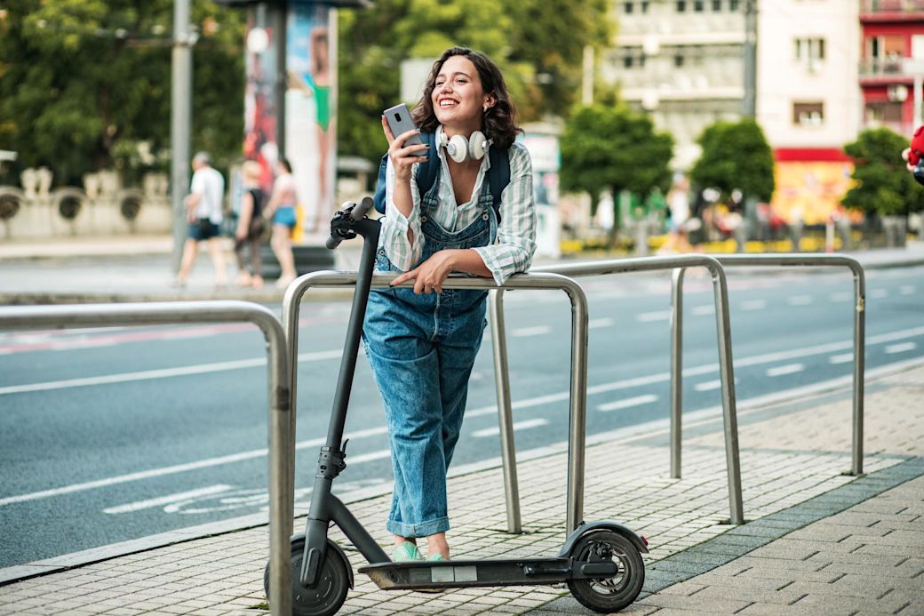 Smart in der Stadt unterwegs mit Elekroscooter Frau mit Smartphone in der Stadt lehnt neben ihrem E-Scooter