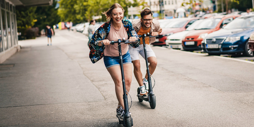 Junges Paar hat Spaß und fährt mit E-Scooter durch die Stadt.