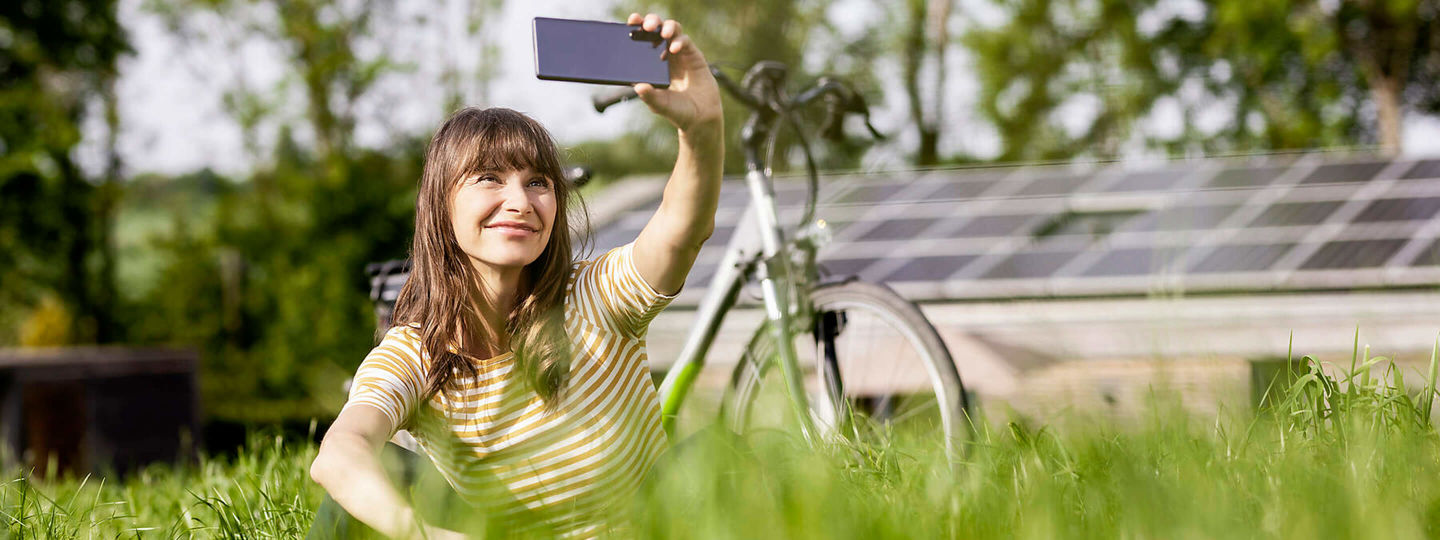 Eine Frau mit Fahrrad macht ein Selfie vor ihrer Photovoltaikanlage