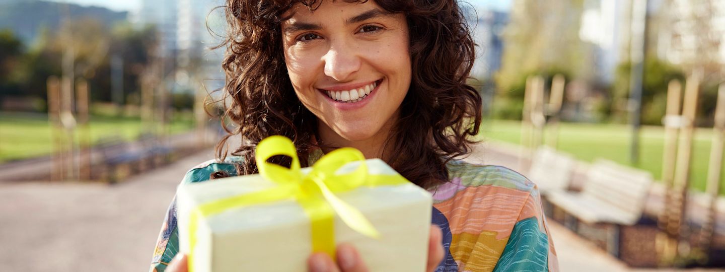 Mit der Yello App Strom und Gas gewinnen. Frau guckt in die Kamera, lächelt und hält Geschenk in der Hand.