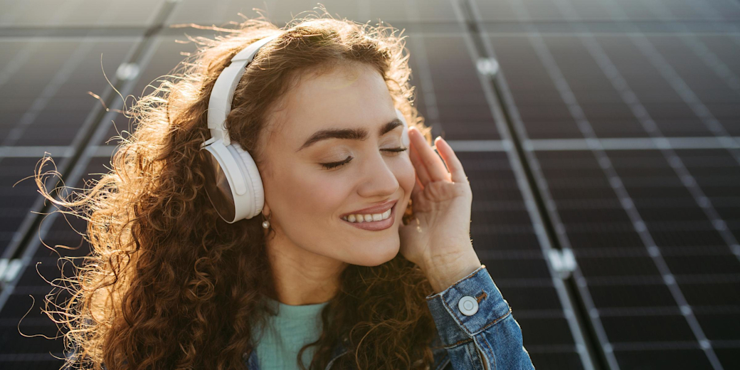 Frau mit Kopfhörern hört Musik vor Solaranlage.