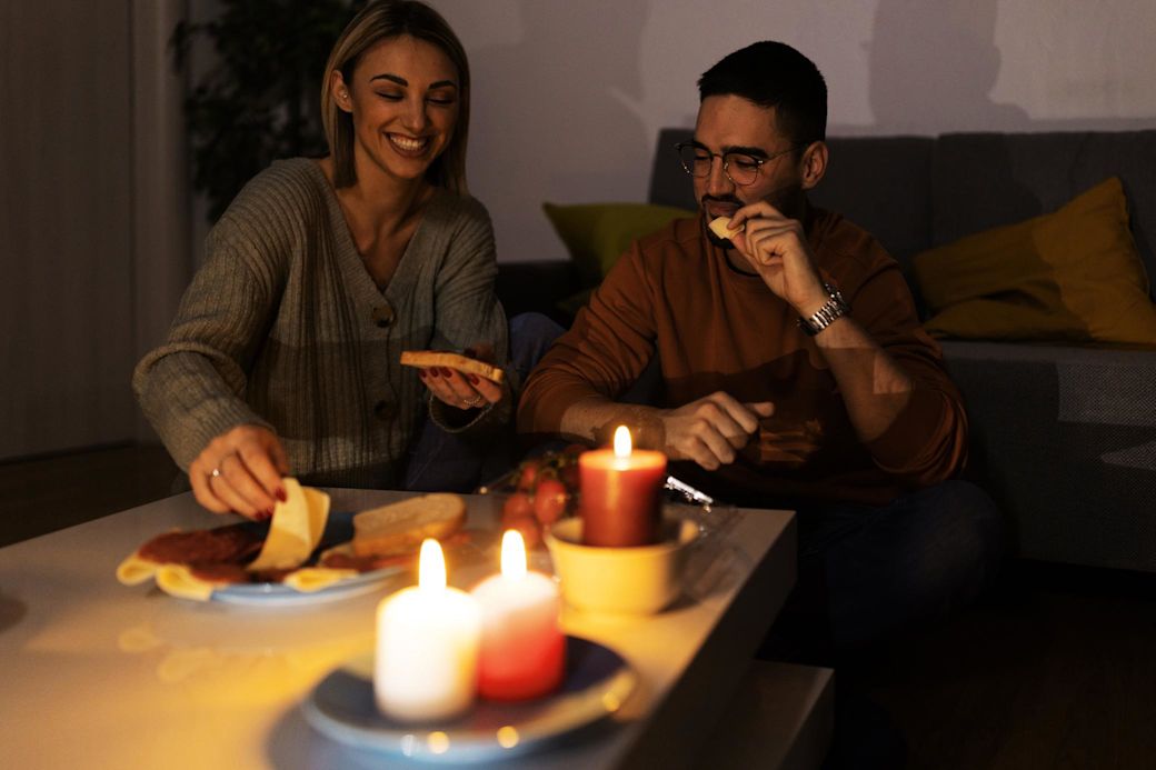 Beim Stromausfall wende dich an deinen Netzbetreiber Paar isst bei Kerzenlicht während eines Stromausfalls
