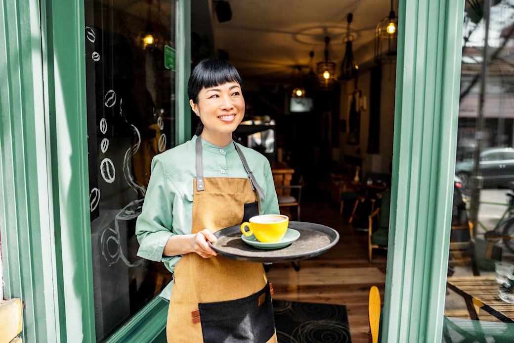 Mit Gewerbestrom versorgst du dein Geschäft günstiger Frau vor einem Cafe mit Tablett und gelber Kaffeetasse