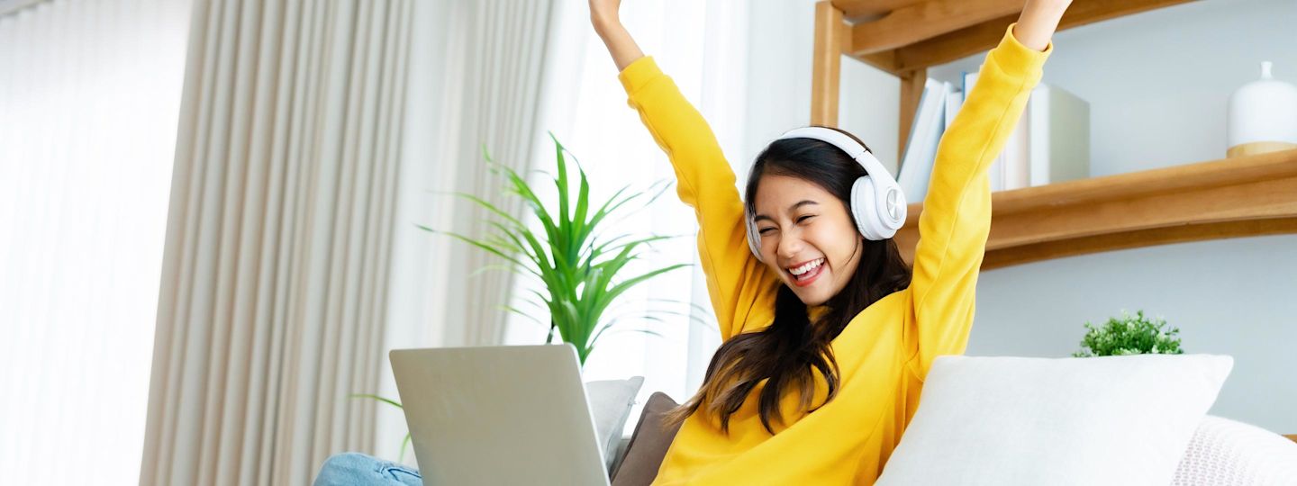 Ganz easy mit Yello Strom sparen. Junge Frau sitzt mit Laptop auf dem Sofa und freut sich