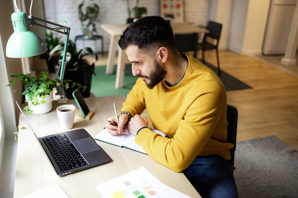 Bleibt gut informiert zu Energie und Klimaschutz Junger Mann am Laptop schreibt in sein Notizbuch