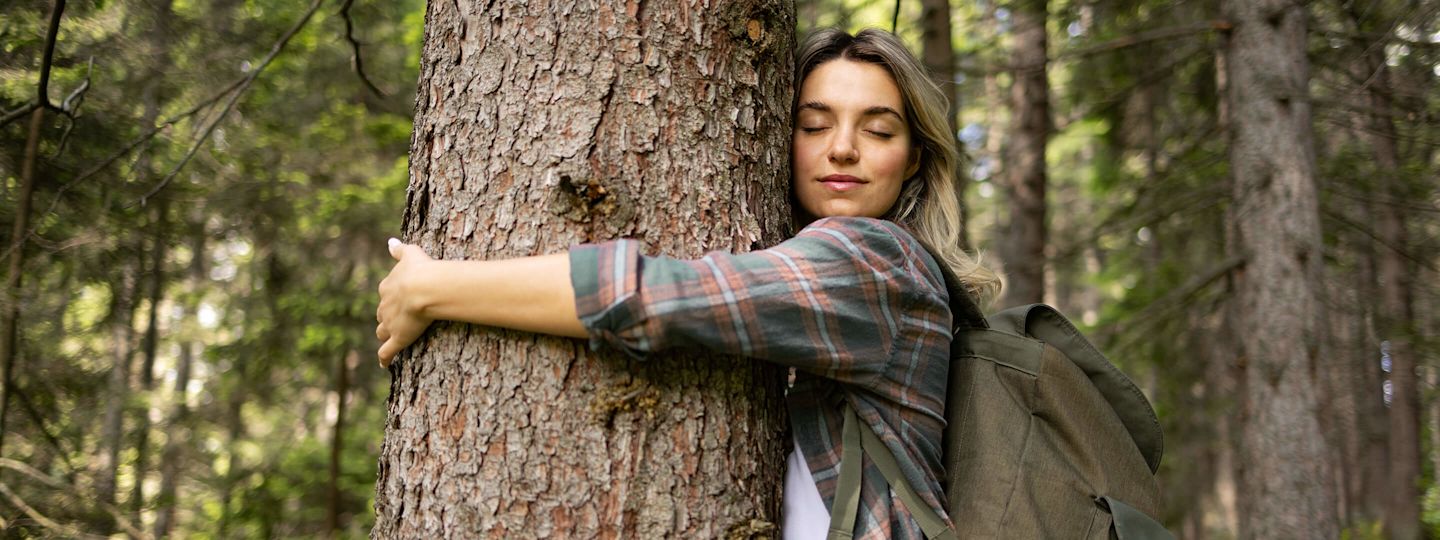 Für mehr Klimaschutz: Extra Abgabe für ausgestoßenes CO₂ Frau steht im Wald und umarmt einen Baum