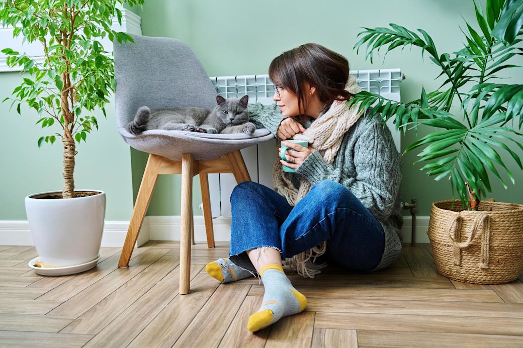 Achte auch in deiner Mietwohnung auf die Heizkosten  Frau sitzt in warmer Kleidung mit Katze vor der Heizung