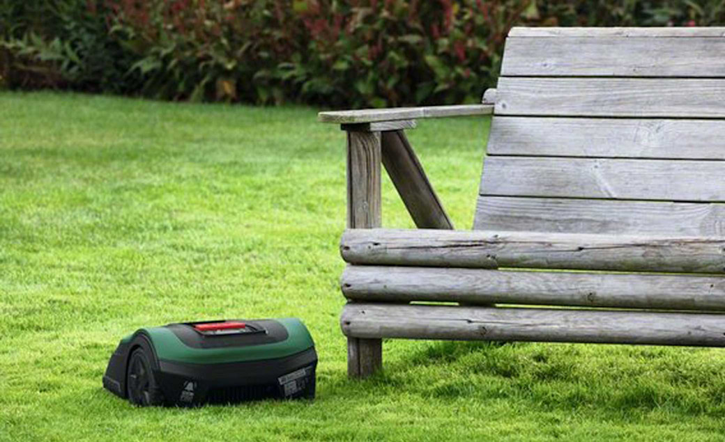 Bosch Rasenroboter Indego XS 300 auf dem Rasen mit einer Holzbank