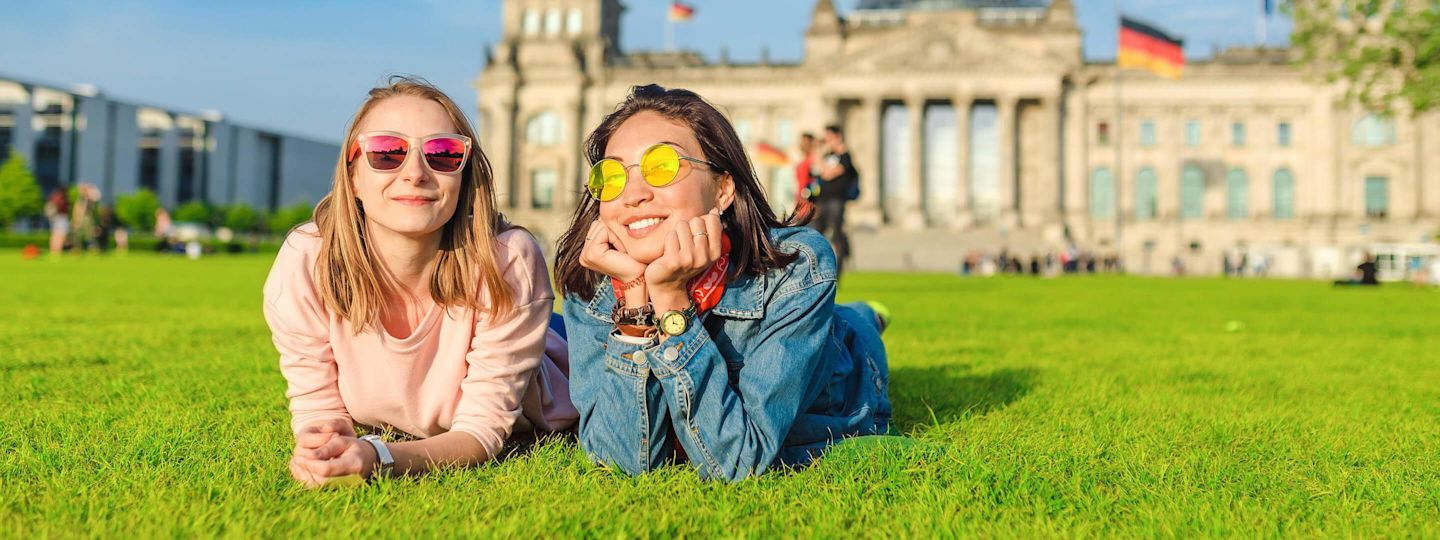 Als dein fairer Gasanbieter sorgen wir für gute Energie in Berlin Zwei Frauen liegen vor dem Reichstagsgebäude in Berlin auf der Wiese
