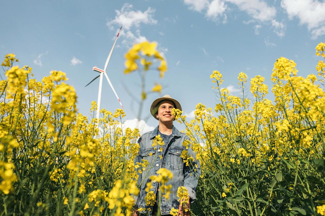 Der Ausbau Erneuerbarer Energien wird gefördert  Junger Mann in Rapsfeld mit Windrad im Hintergrund