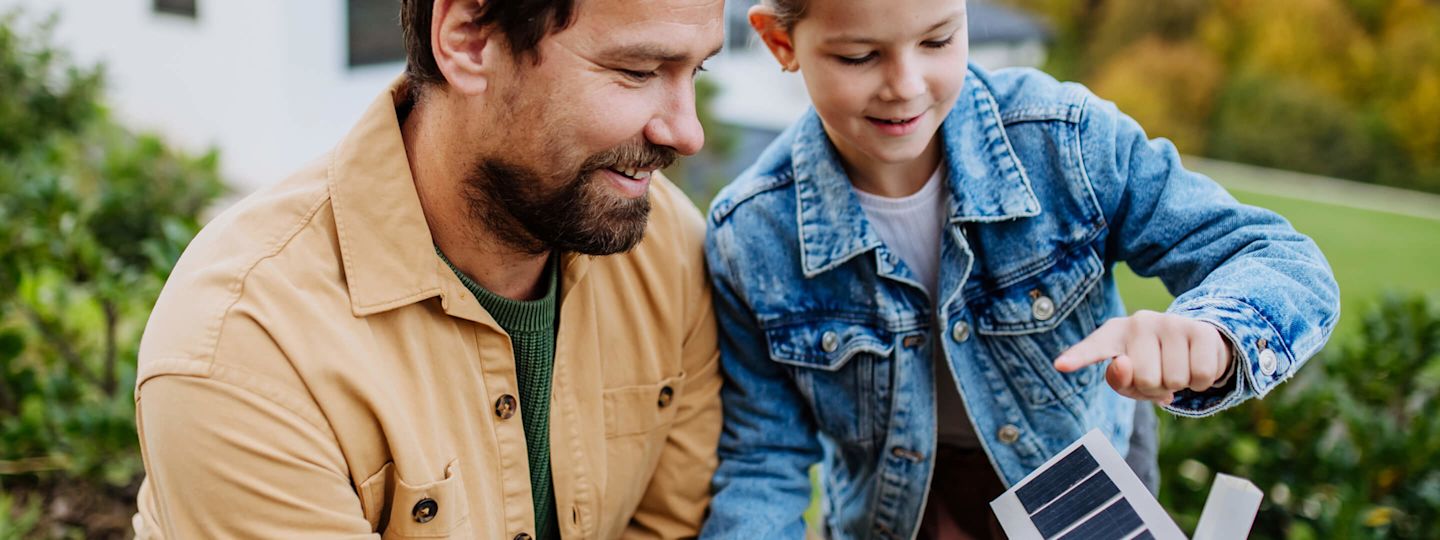 PV-Anlage planen. Wir erklären dir wie. Kleines Mädchen mit ihrem Vater, die anhand eines Papiermodells ihr Haus mit Solarmodulen planen.
