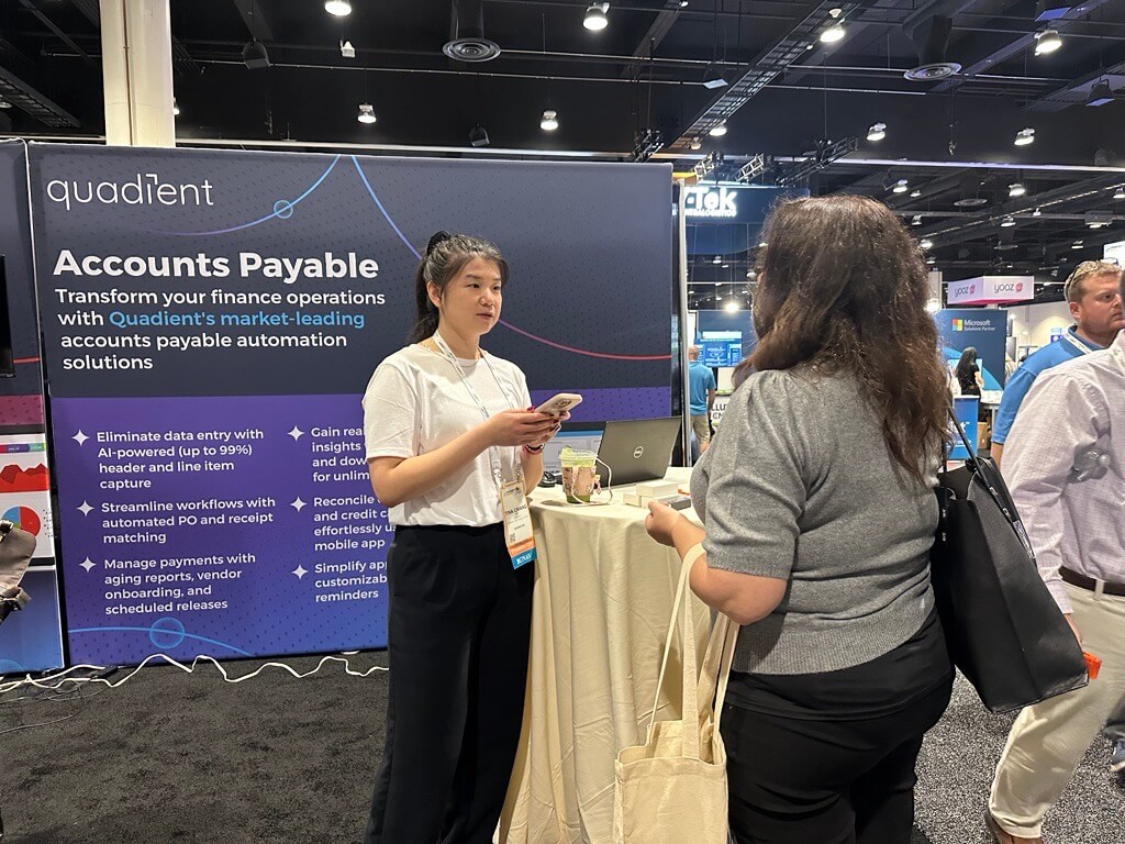 Two people are standing and conversing at a trade show booth for Quadient.