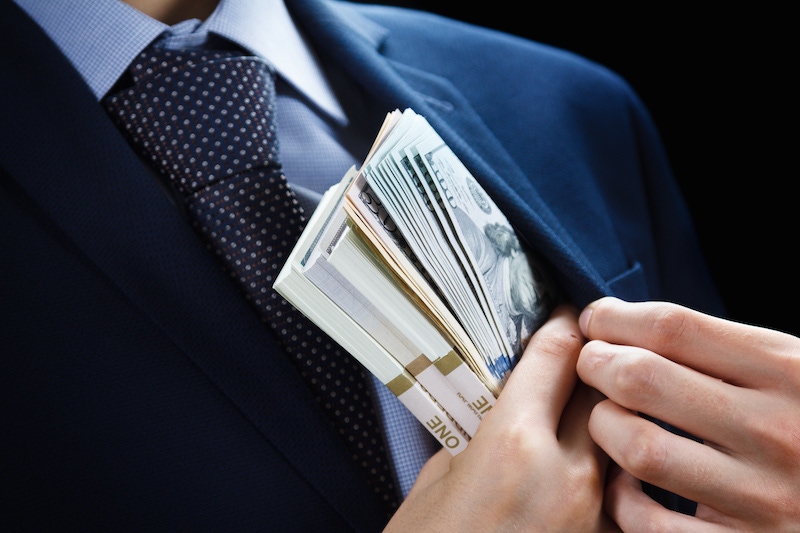 businessman putting dollar bills into his jacket