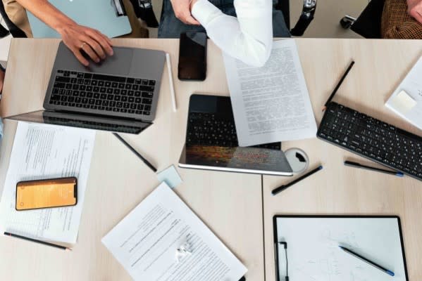 Two people are working on their laptops, and there are some pages adjacent to their laptops