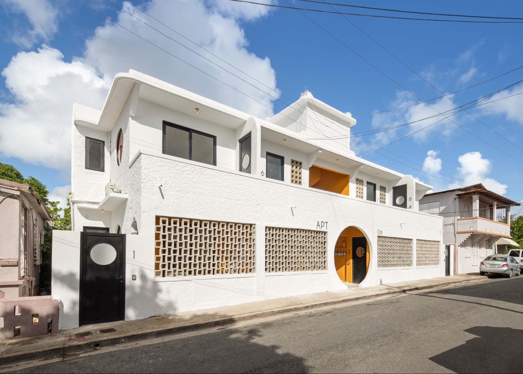 Exterior view of a modern two-story white building featuring geometric architectural details, decorative breeze-block screens, and circular yellow doorway accents.