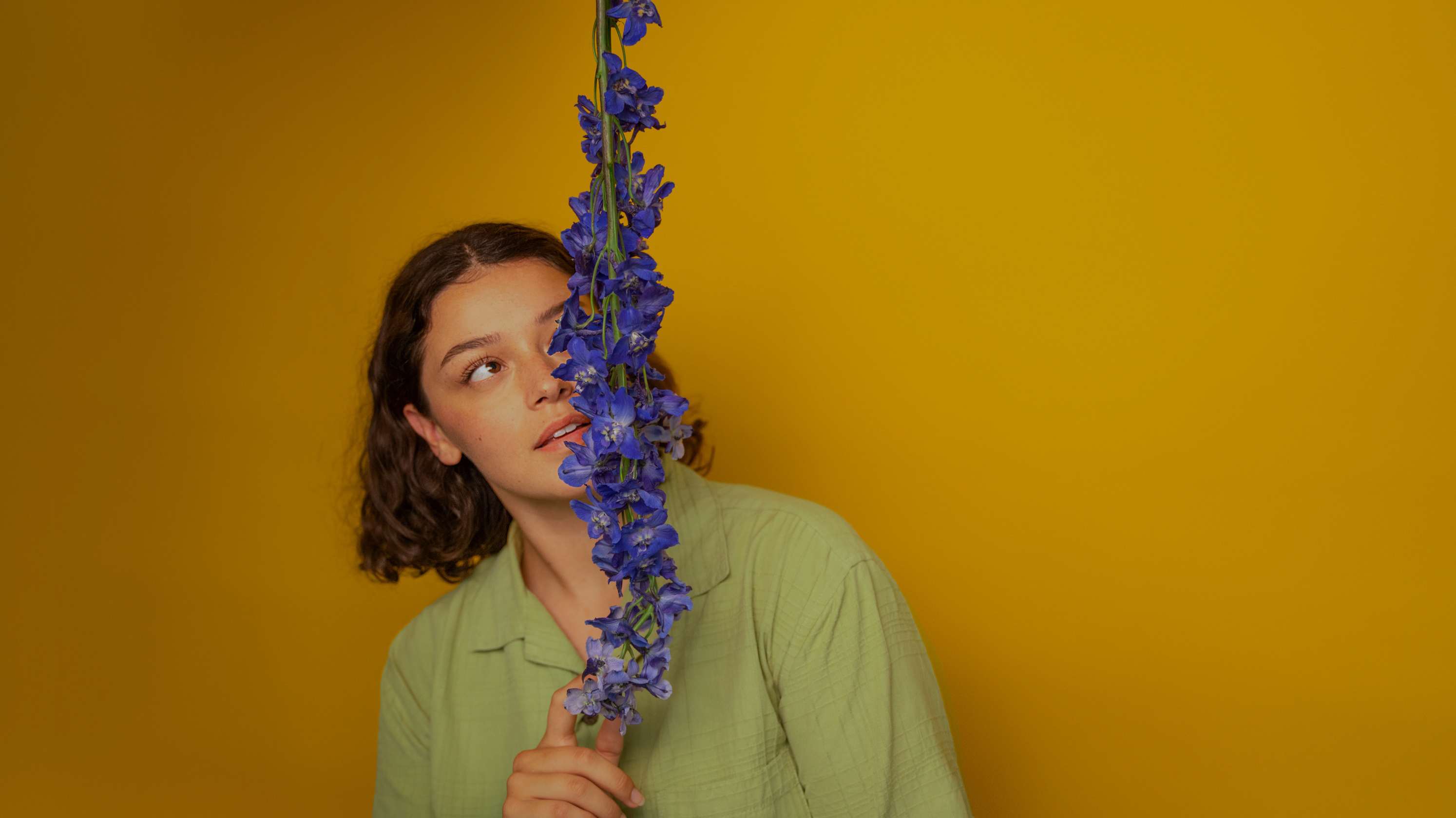 woman holding a stalk of purple flowers against a yellow background