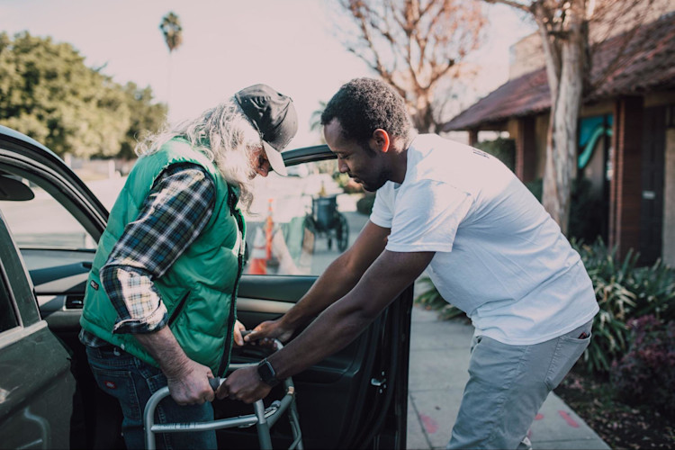 Man assisting an old man out of a car.