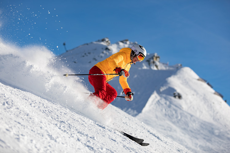 Person in yellow jacket and red pants skiing down mountain