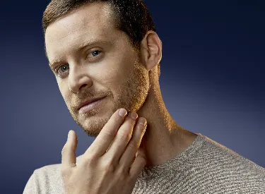 Person wearing gray sweater touching jawline against dark blue background