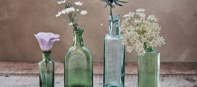 Quatre bouteilles différentes et colorées en verre contenant diverses fleurs