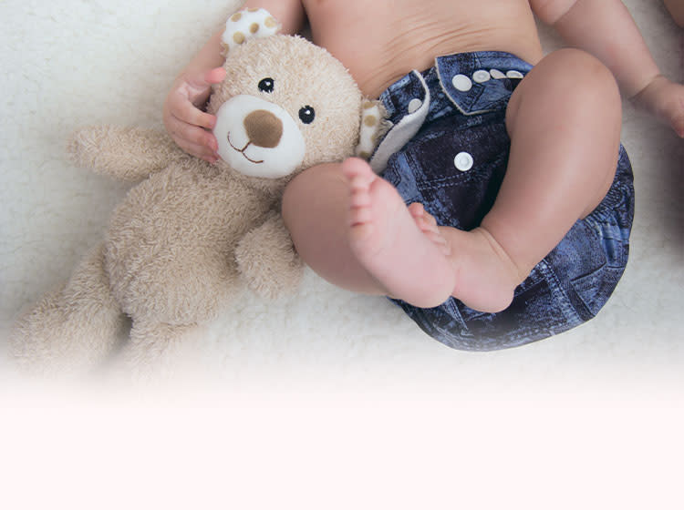 The baby lies on the carpet, holding a toy with his hand