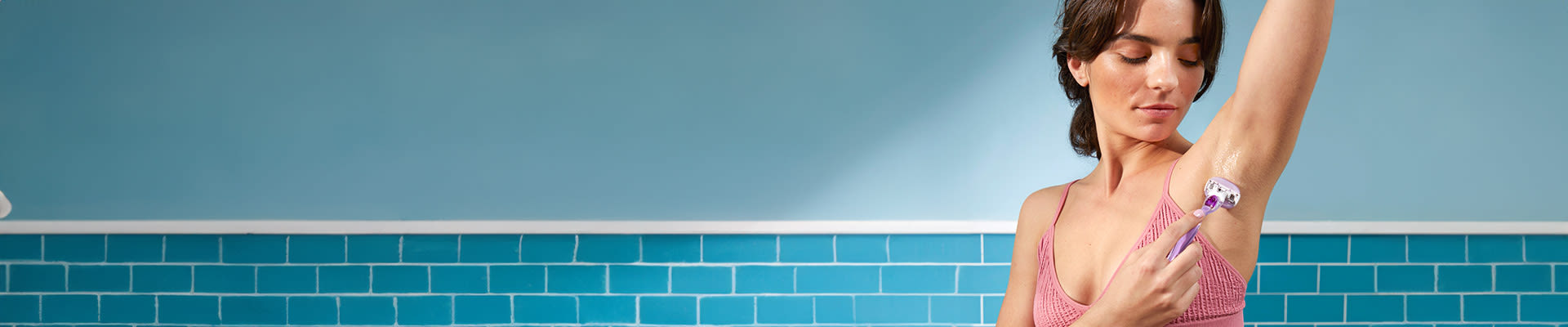 Donna in bagno seduta su una vasca da bagno e che si rade l'ascella.