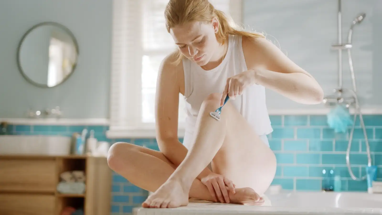 Donna seduta sul pavimento del bagno che si rade le gambe con il rasoio Gillette Venus