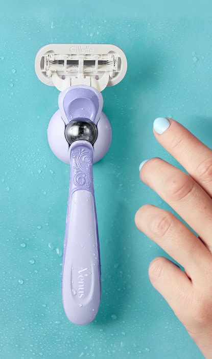 Mano femminile che raggiunge il rasoio ricaricabile Gillette Venus Extra Smooth Swirl sul supporto della doccia