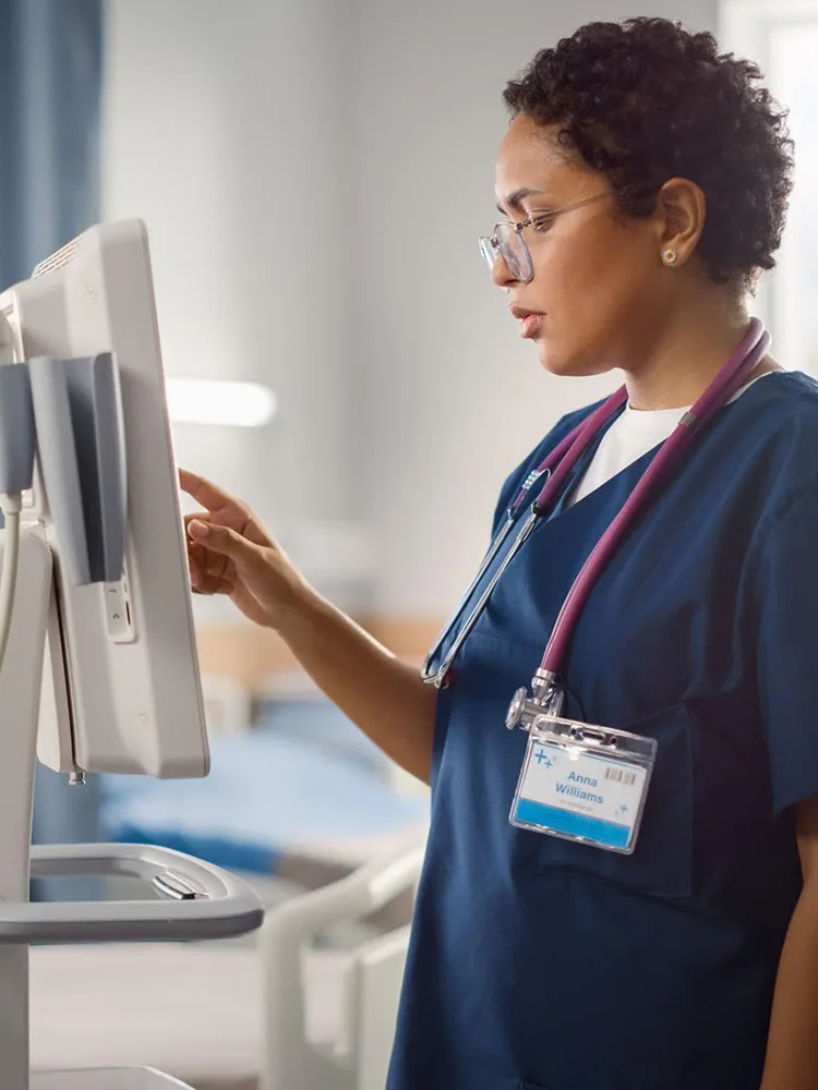 clinician in scrubs with the stethoscope stands working at a computer