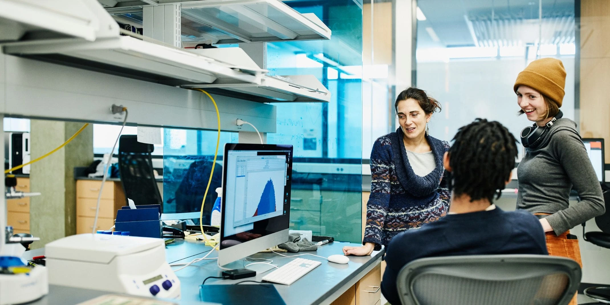 Group of scientists chat around desk, in the lab