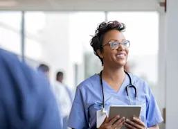 Nurse stands with tablet computer smiling