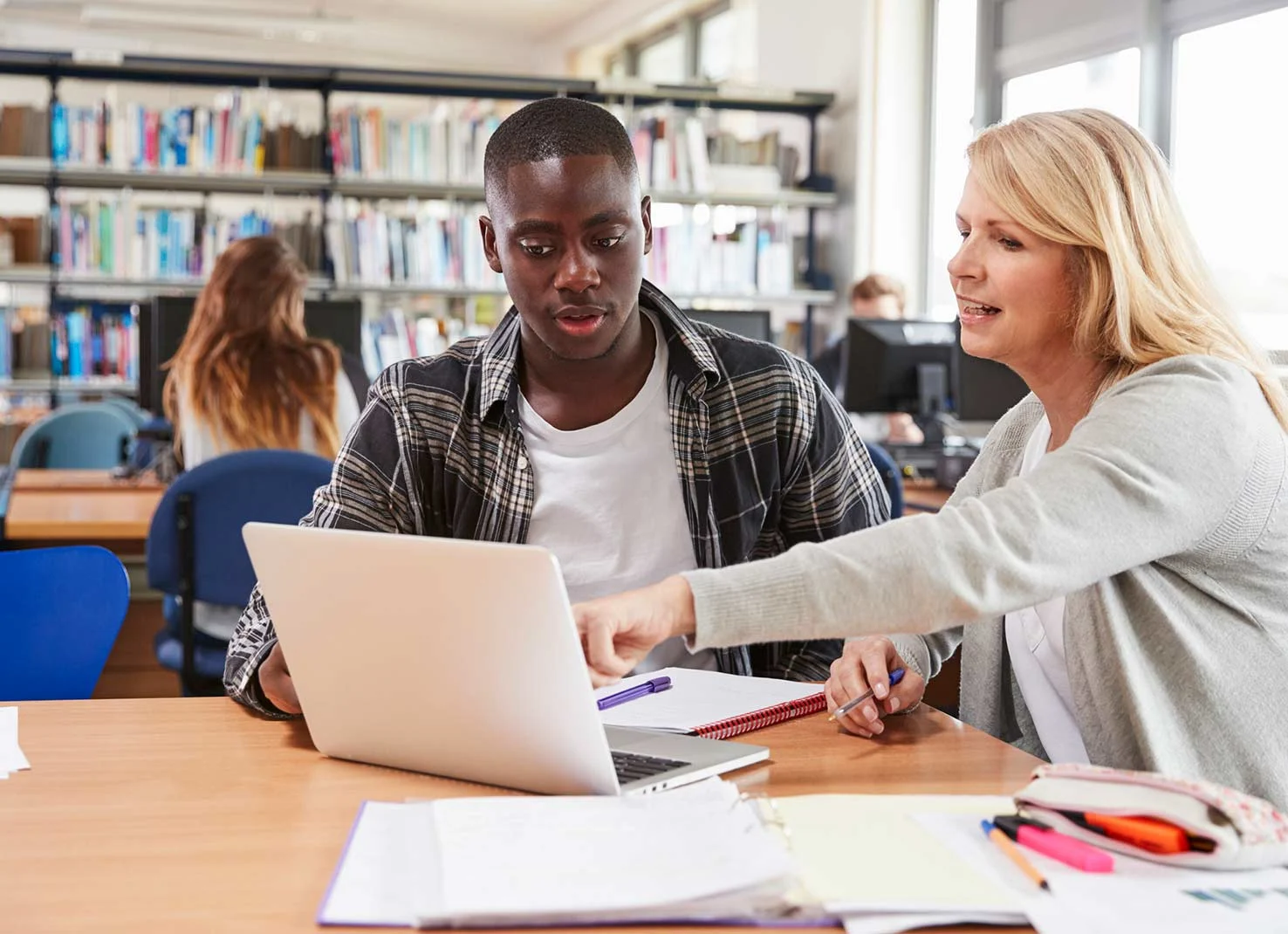 Teacher helps students with laptop in a library.