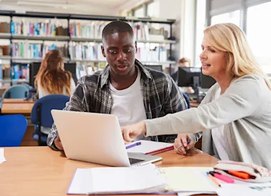 Group of students with teacher pointing at laptop