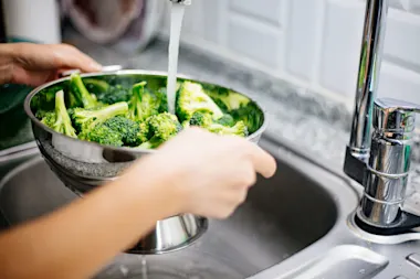 Person washing broccoli in a colander under running water
