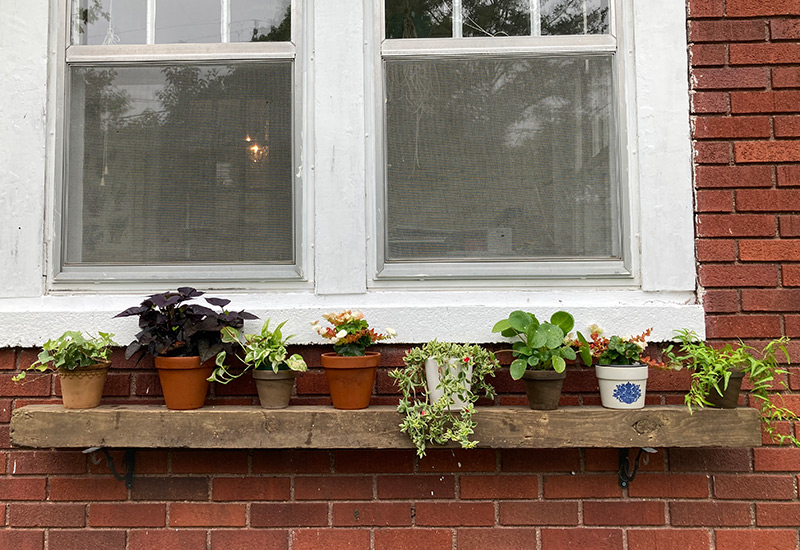 Houseplant Shelf: A worn piece of lumber and some brackets make an easy outdoor shelf for displaying houseplants.