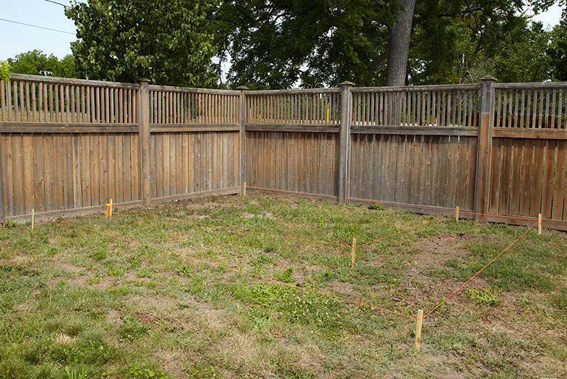 Before photo of space where installing paver patio: Measure the space for the patio and mark it out with stakes and twine.