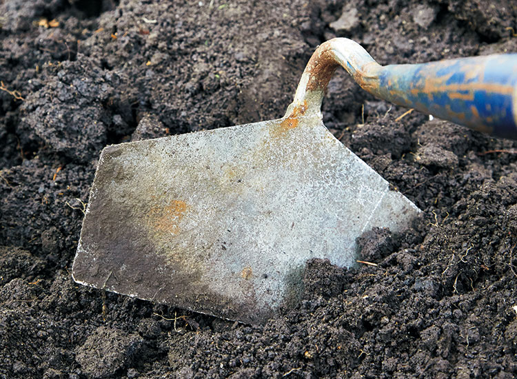 Closeup of draw hoe breaking up soil: Draw hoes are a good all-purpose tool but best for large-scale tasks. 