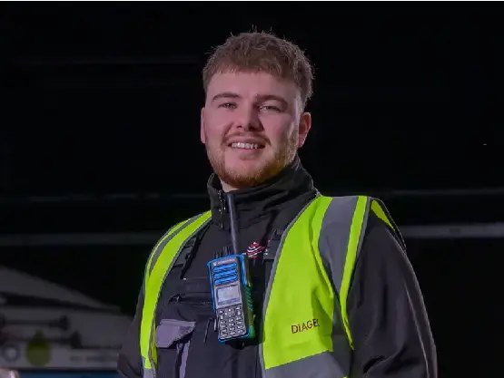A young man stands next to some whisky barrels.