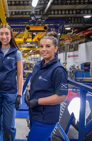 Two young women stand next to an aircraft part.
