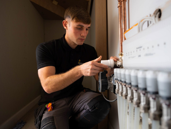 A young man crouches down while turning a heating valve