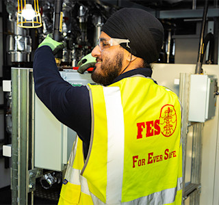 Young smiling man in high-vis waistcoat operating a machine in an industrial building